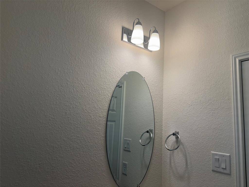 This photo shows a half bathroom corner featuring a textured wall with an oval mirror, modern light fixture above, and a towel ring beside it.