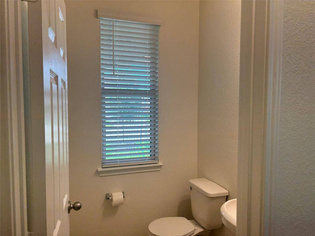 Compact half bathroom downstairs with a window, featuring blinds, a toilet, and a pedestal sink.