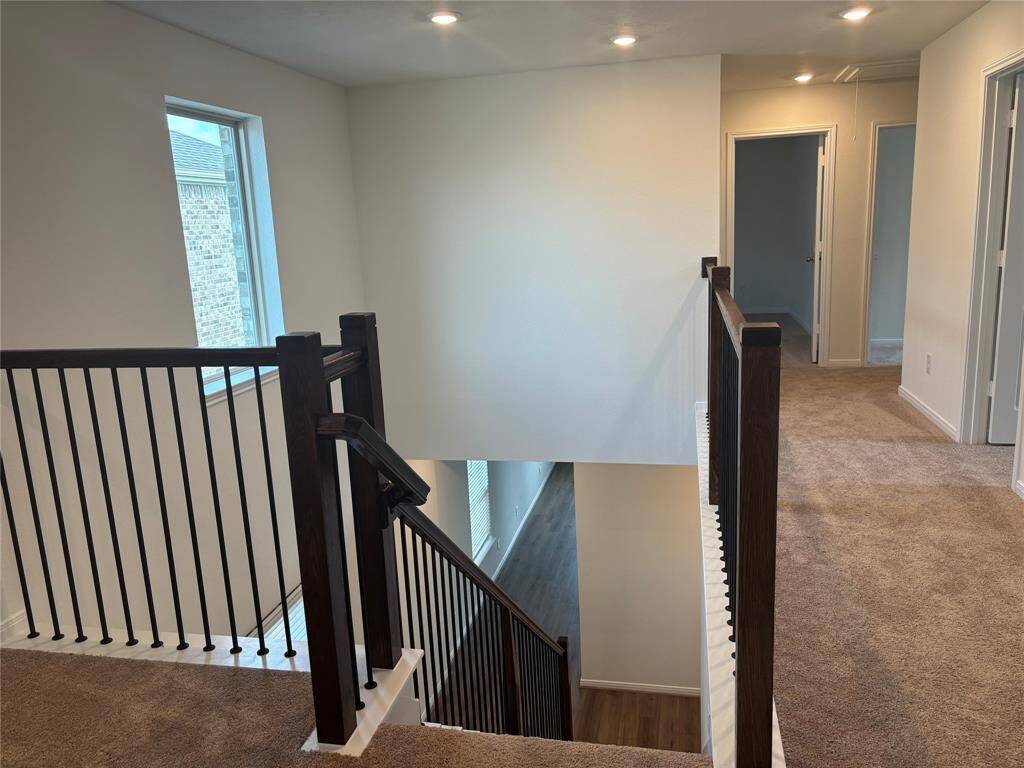 This photo shows a well-lit upstairs landing with carpeted floors and a staircase featuring a dark wood railing and black spindles. There are multiple doorways leading to adjacent rooms, highlighting a spacious and accessible layout.