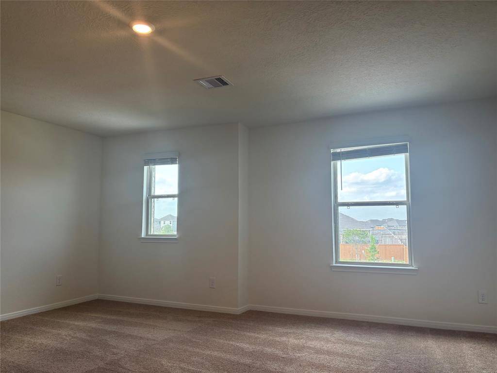 Bright, spacious game room with two windows providing natural light. It features neutral carpeting and a simple ceiling light, creating a cozy and inviting atmosphere.