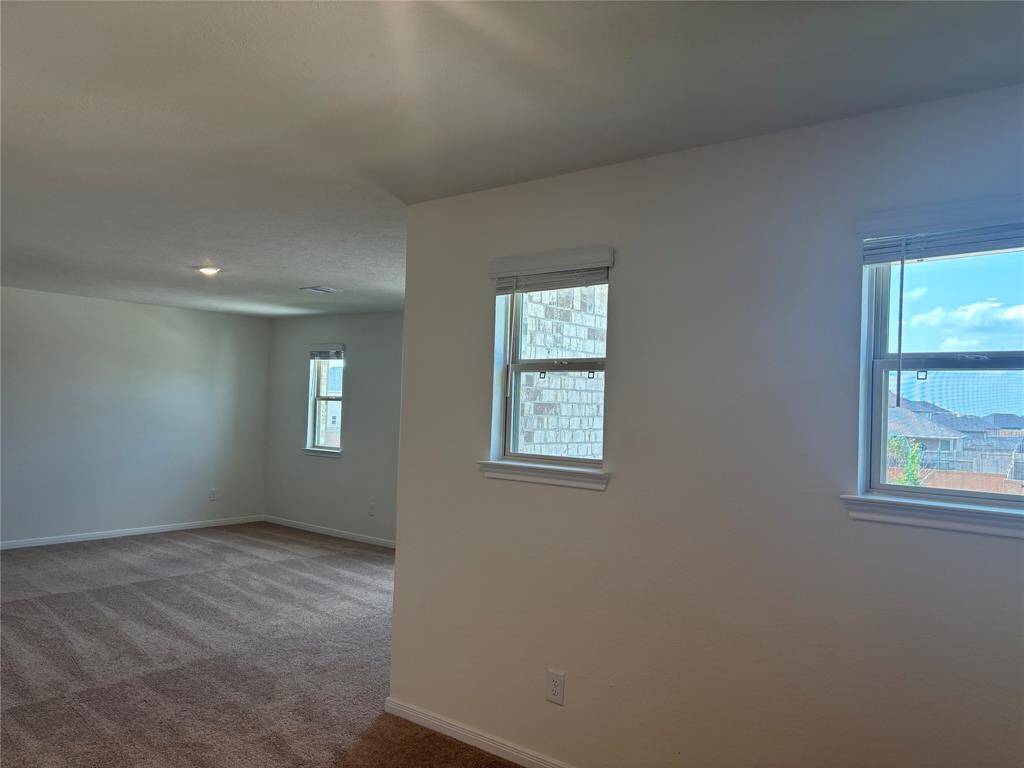 Bright, spacious game room with neutral walls and carpeted flooring. Multiple windows provide ample natural light and offer views of the outdoors.