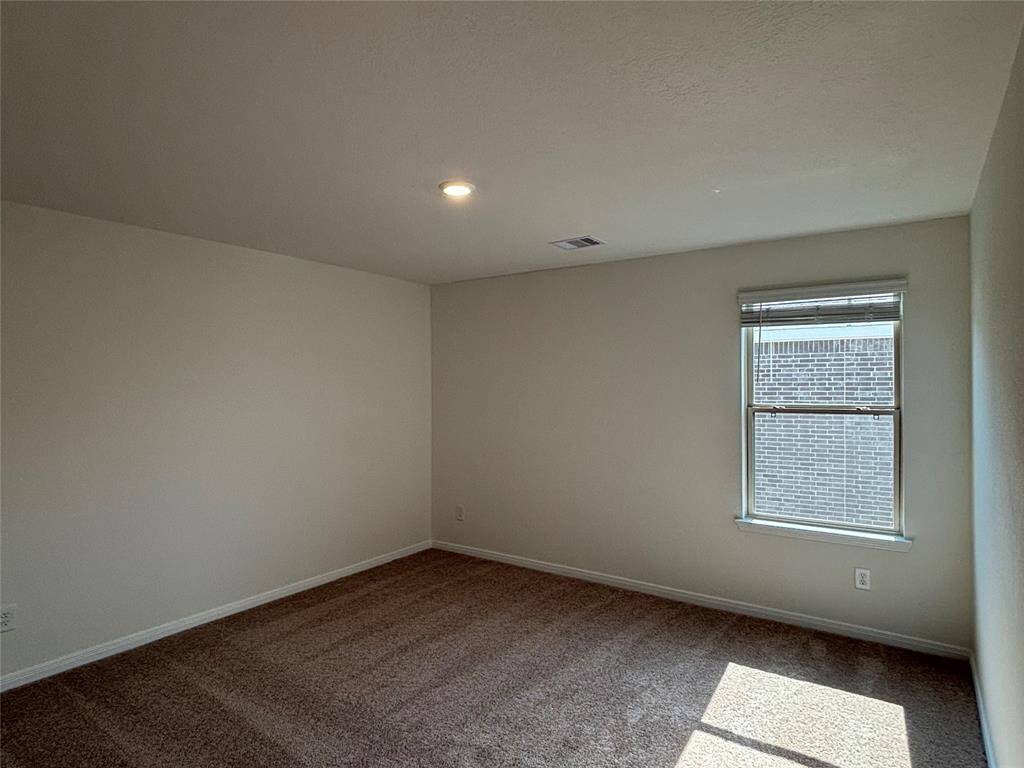 This third room upstairs features neutral walls, carpet flooring, a single window with blinds, and recessed lighting, creating a cozy space with natural light.