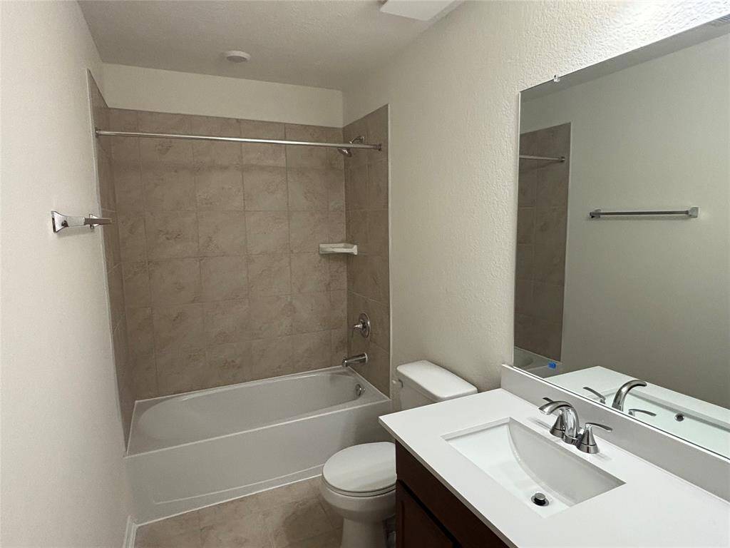 This photo shows a clean, modern second bathroom featuring a bathtub with tiled walls, a sleek vanity with a white countertop and built-in sink, and a large mirror. The space is bright and well-maintained, with neutral colors.