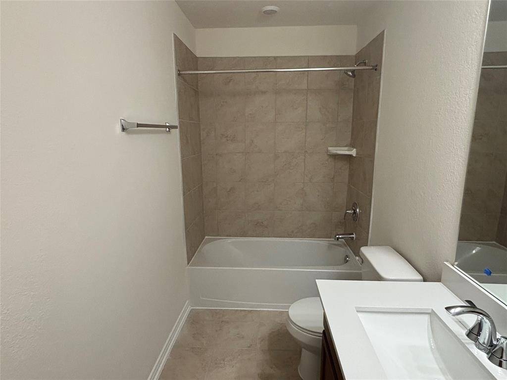 This secondary bathroom features a modern design with a tiled shower and bathtub combo, a sleek vanity with a sink, and neutral-color walls and flooring.