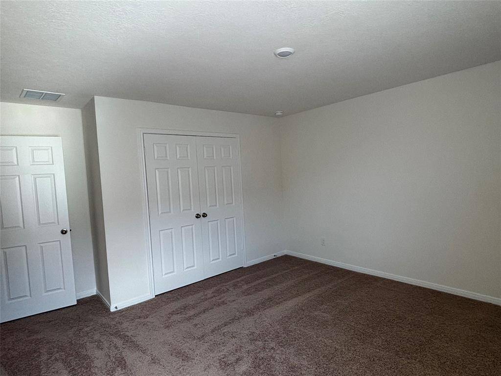 This third room features neutral walls, plush carpeting, and a double-door closet, offering a spacious and versatile area ideal for a bedroom or home office.