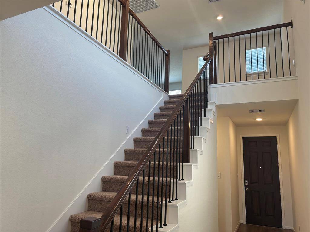 This photo showcases a modern entryway with a carpeted staircase featuring dark wooden railings and black metal balusters. The area is well-lit, and there's a dark front door that complements the staircase design.