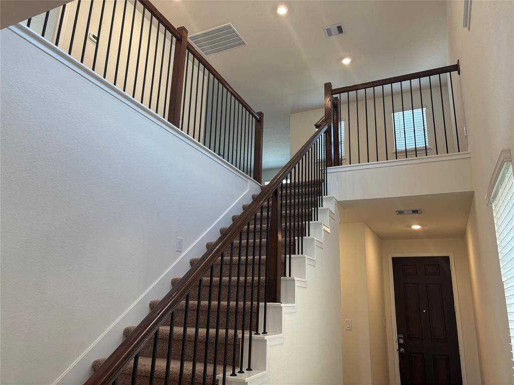 This home features a spacious entryway with a carpeted staircase leading to an upper level. The wooden handrails and metal spindles add a touch of elegance, and the space is well-lit with recessed lighting.