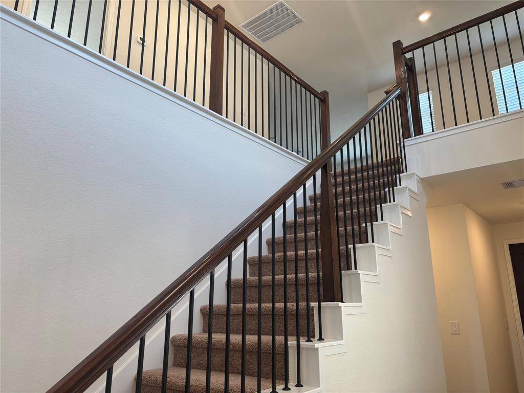 This photo showcases a modern staircase with carpeted steps, dark wooden handrails, and vertical metal balusters. It leads to an upper landing with natural light from a window, creating an inviting and open space.