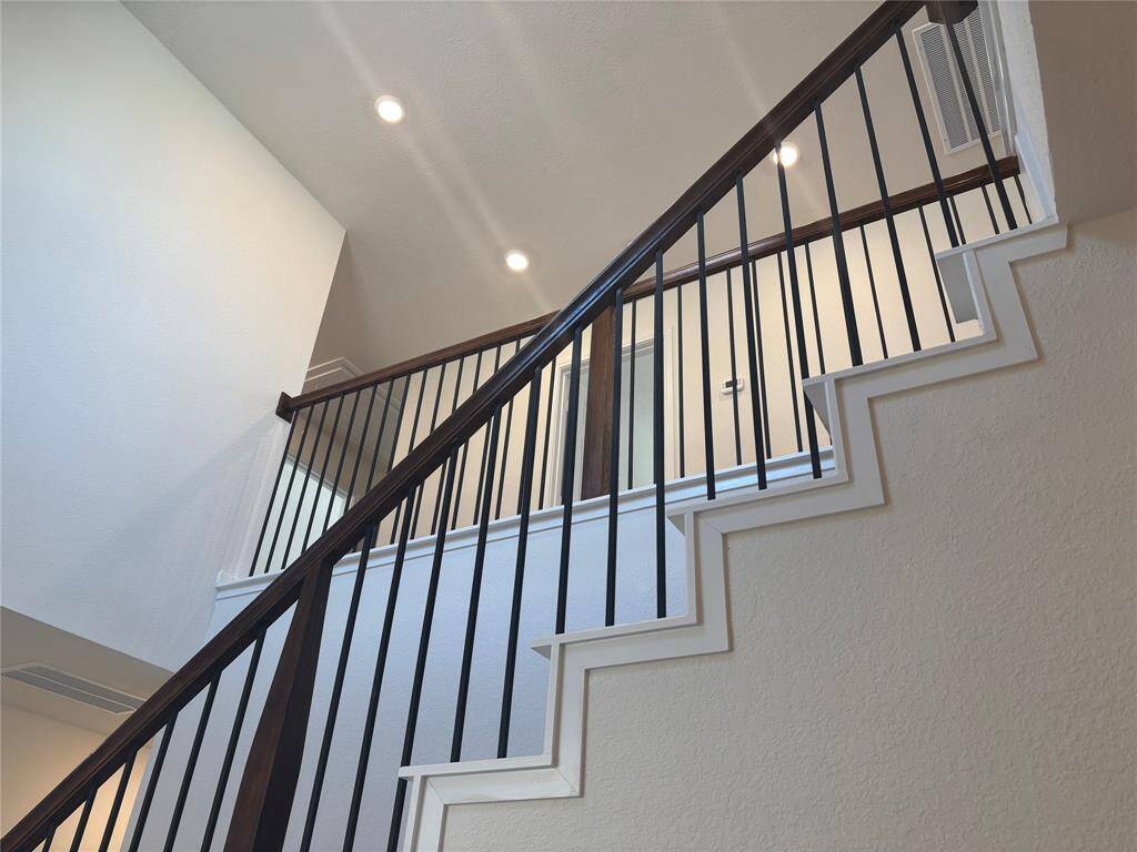 This photo features a modern staircase with sleek, dark metal railings and a light, neutral wall color, creating an elegant and open feel in the home. Recessed lighting adds a bright and inviting ambiance.