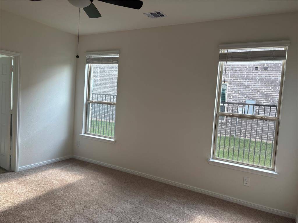 Bright primary room downstairs with neutral walls and carpet. Features two large windows allowing natural light and a ceiling fan. Access to a small adjacent area or room.