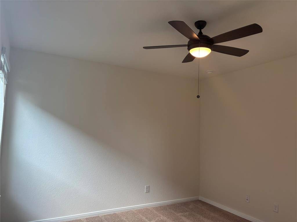 This primary room downstairs features a neutral-toned carpet and walls, a ceiling fan with a light fixture, and natural light from a window. It's a clean, versatile space suitable for various purposes.