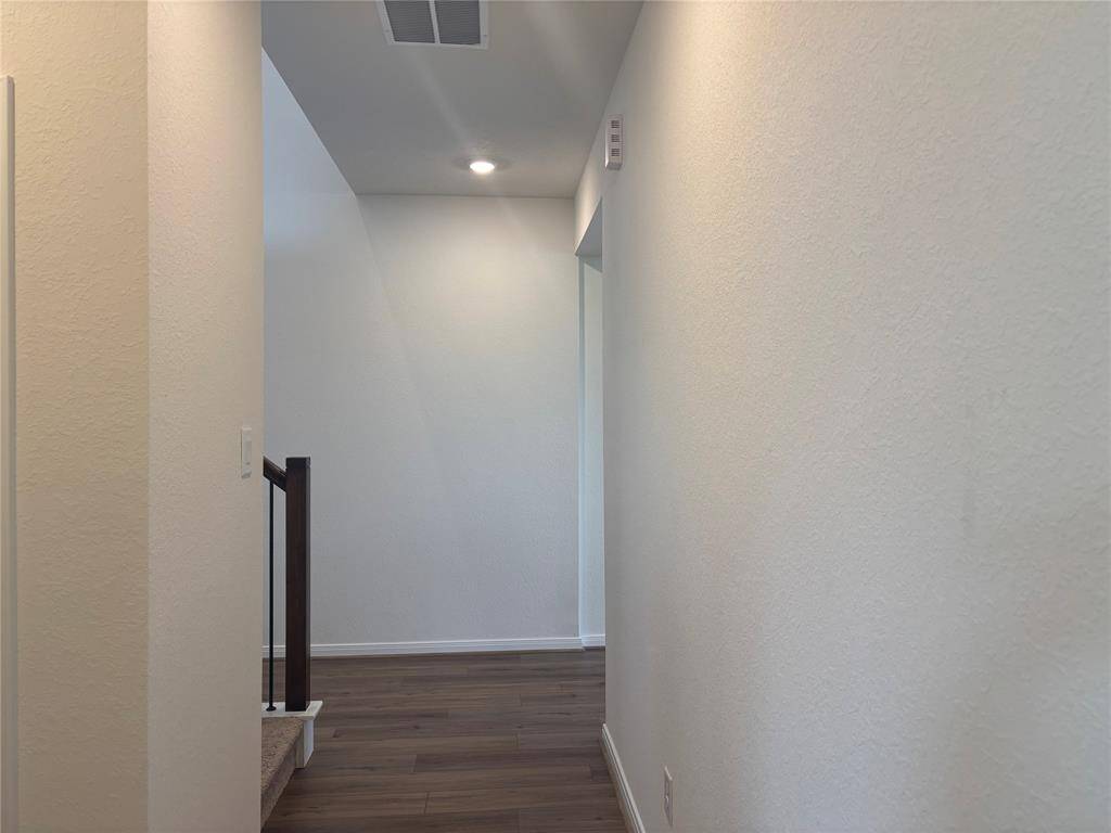 This photo shows a clean, narrow hallway with light-color walls and wood flooring. It features a staircase with a dark railing and recessed lighting, creating a bright and open feel.