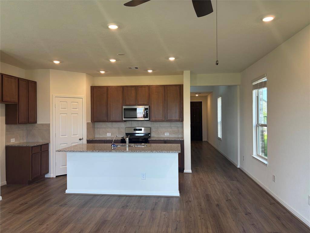 This photo showcases a modern kitchen with wood flooring, sleek cabinetry, and granite countertops. It features a central island with a sink, stainless steel appliances, and recessed lighting, creating a bright and inviting space.