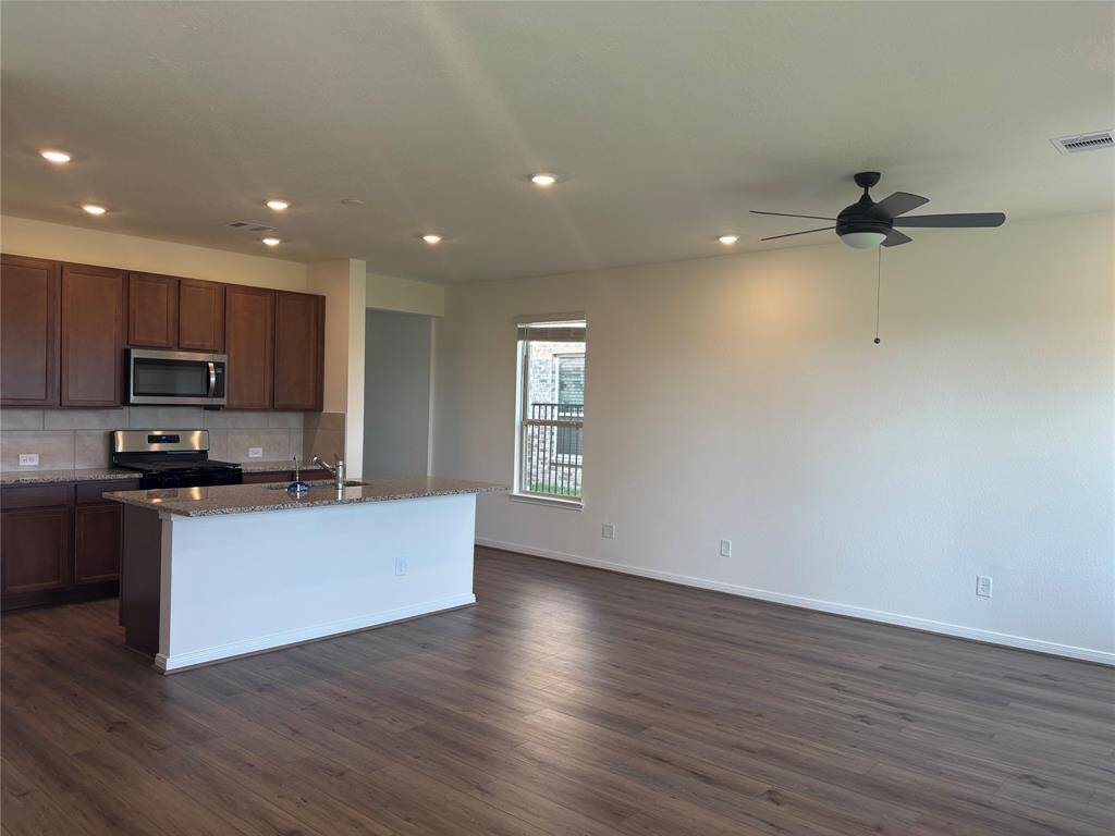 Bright, open-concept kitchen and living area with wood flooring, granite countertop, stainless steel appliances, recessed lighting, and a ceiling fan.