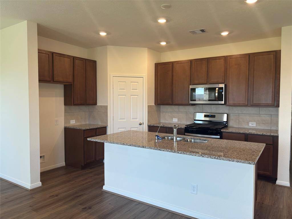 This modern kitchen features sleek granite countertops, ample wooden cabinetry, stainless steel appliances, and a spacious island with a double sink, perfect for meal preparation and entertaining.