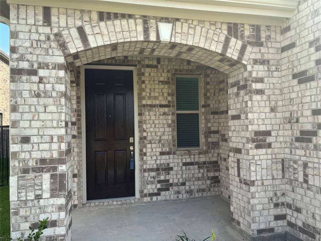 This photo showcases a charming brick front porch with an arched entryway, featuring a dark wooden door and a window with shutters. The space offers a welcoming and sheltered entrance to the home.