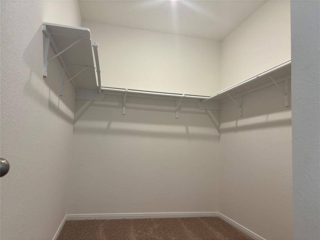 This Primary Bedroom closet shows a spacious walk-in closet with carpeted flooring, white walls, and multiple shelves and hanging rods for ample storage.
