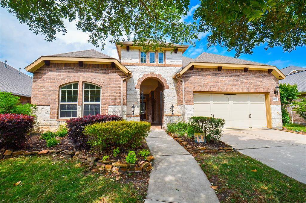 The long paved walkway brings us to the covered front entrance, where the artisan-like brick/stucco facade delights with a Mediterranean flair. The pristine attached garage, right, sits above the easily accessible driveway.