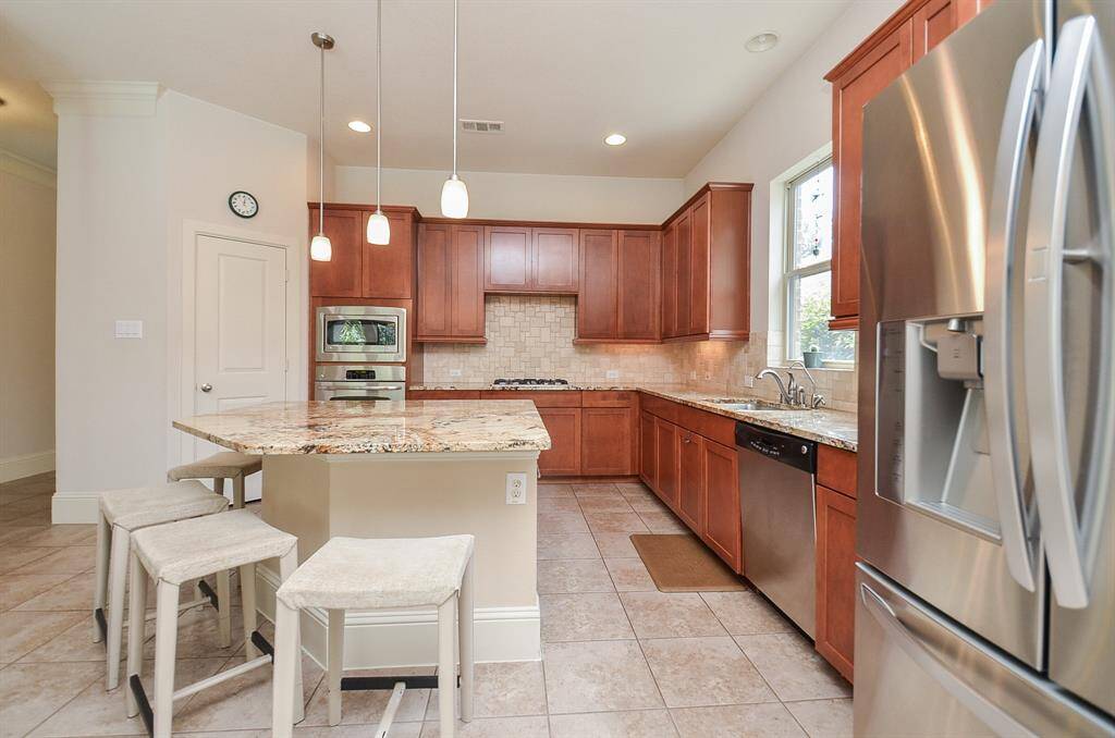 The custom shape and structure of this island is something you won't see everywhere. Clever angles and extended counter top invite multiple stools, with sleek angles facing the kitchen; and it's array of honey toned cabinetry, up and down, pale granite counters, complemented by good looking tile backsplash.