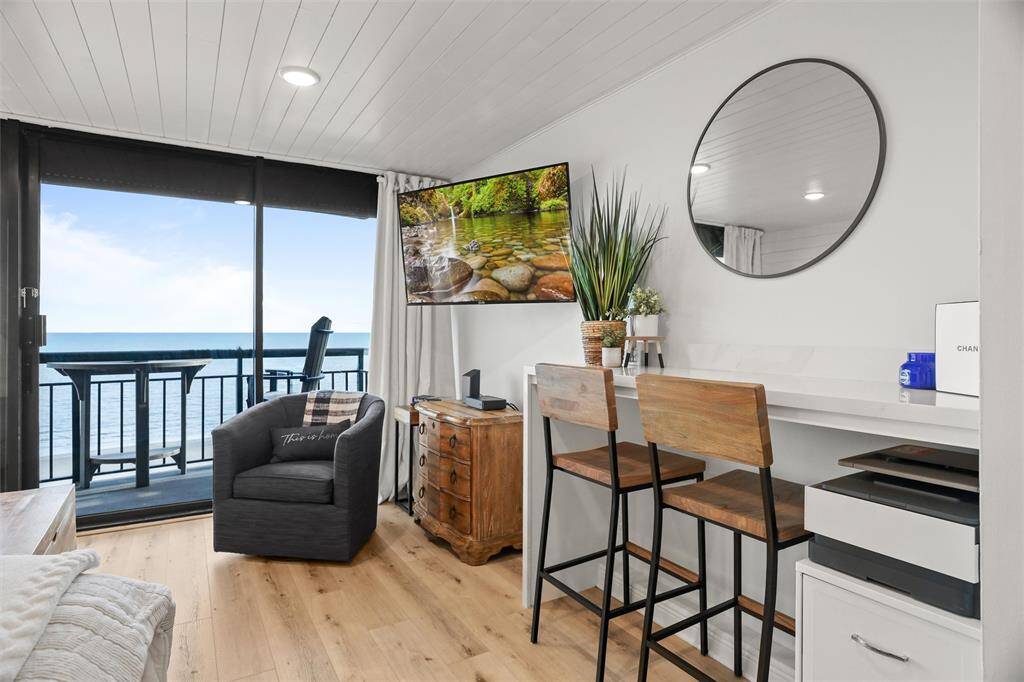 Contemporary coastal-style space featuring a comfortable seating area, a sleek work nook with bar seating, and a breathtaking ocean view from the balcony.