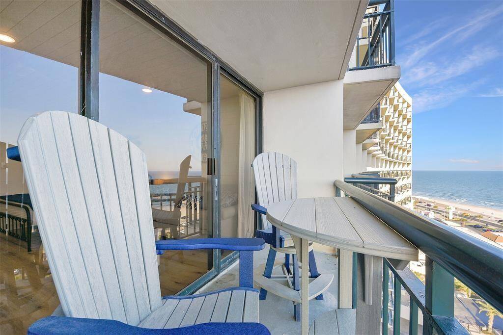 This is a balcony with a seaside view, featuring two tall Adirondack style durable polywood chairs and a table, ideal for enjoying the coastal scenery and fresh air.