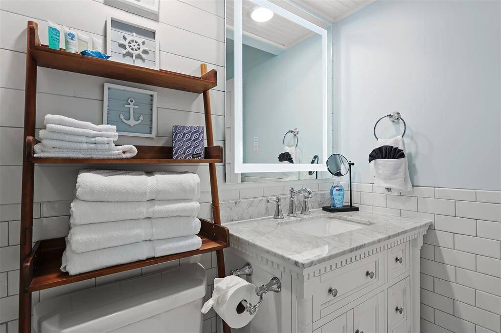 Anti fog lighted mirror over quartze counter and white vnity. Extra storage with attractive shelving.