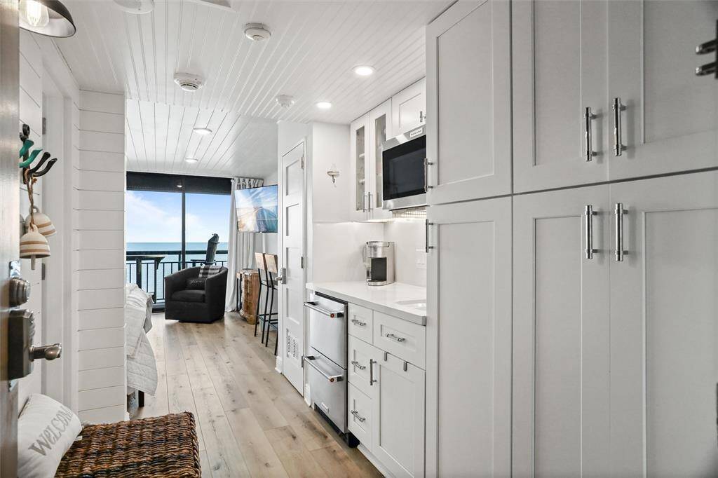 You're looking at a sleek, modern kitchen with white shaker cabinetry and stainless steel appliances, opening up to a cozy living space with a stunning ocean view from the balcony. New Coffee maker and cooktop not pictured.