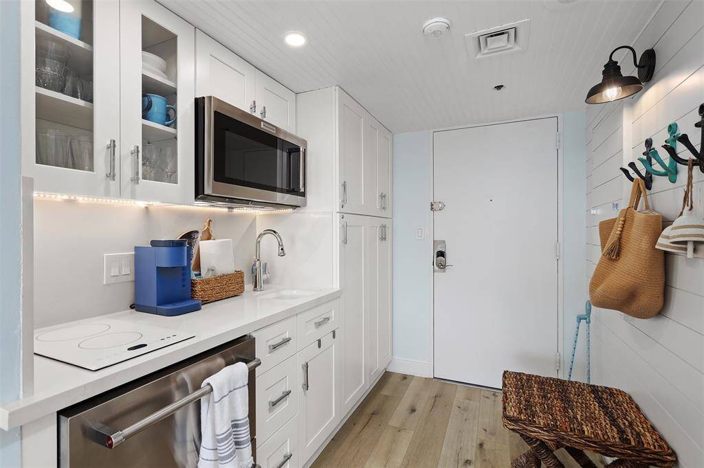 This is a modern kitchen with white shaker style cabinetry, stainless steel Kitchenaide appliances, under-cabinet lighting, and sleek Quartze countertops with a backsplash. There is a built-in microwave, glass-front upper cabinets, and builit in mini frig/freezer with ice maker.