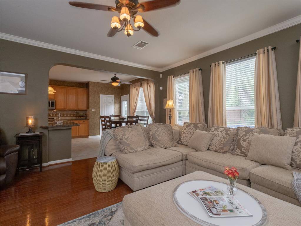 This inviting family room features warm wood flooring, and ample natural light from multiple windows. The open layout seamlessly connects to a cozy kitchen with wood cabinetry and the breakfast area, creating a perfect environment for relaxation and entertaining.
