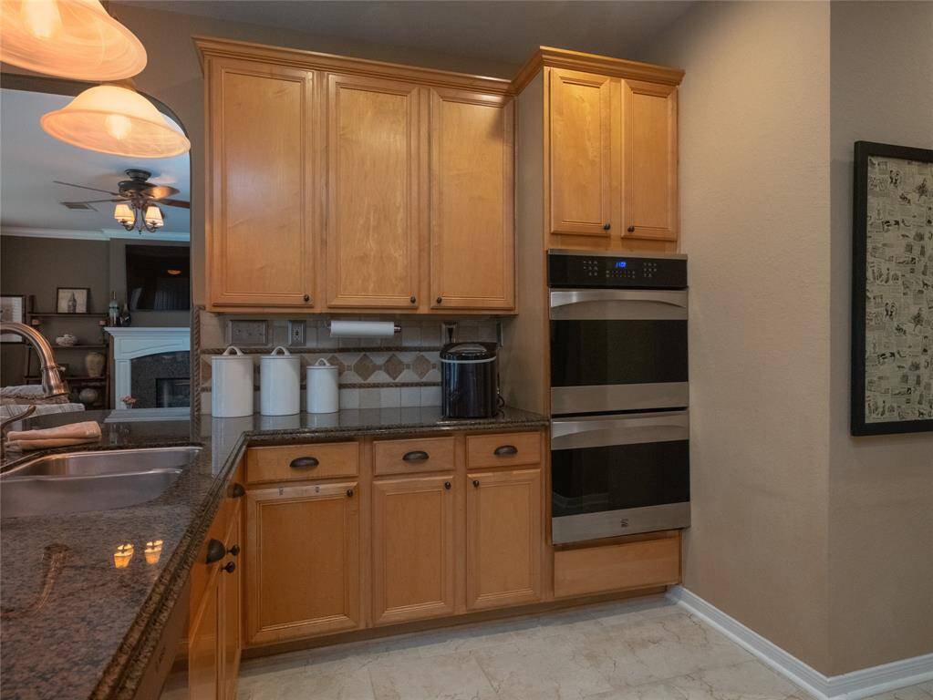 Love the openness of this kitchen that features warm wood cabinetry, granite countertops, double ovens, and a tile backsplash. It connects to a cozy family room with a fireplace, creating a welcoming, open-concept space.