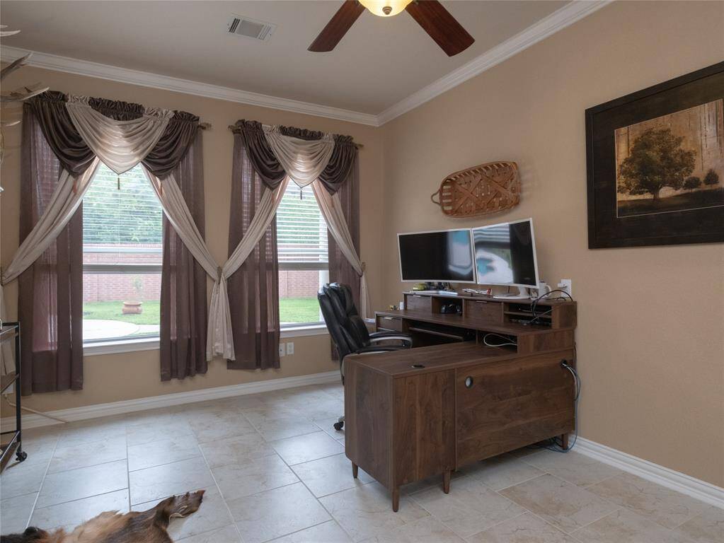 This spacious study or bonus room features tiled flooring and a large window with elegant drapes, offering ample natural light. The neutral wall color adds warmth, complemented by tasteful decor.