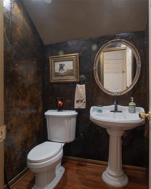 This stylish half-bathroom with dark textured walls, a round mirror, and a classic pedestal sink is right off the front foyer near the family room.