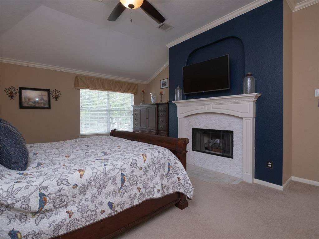 This ample primary bedroom features a vaulted ceiling, a cozy fireplace with a dark blue accent wall, and a large window providing natural light.