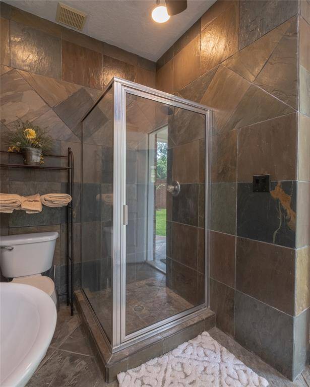 You will enjoy this modern glass shower with elegant slate tile walls and flooring. It includes a white toilet and sink, with a towel rack and decor adding a warm touch.
