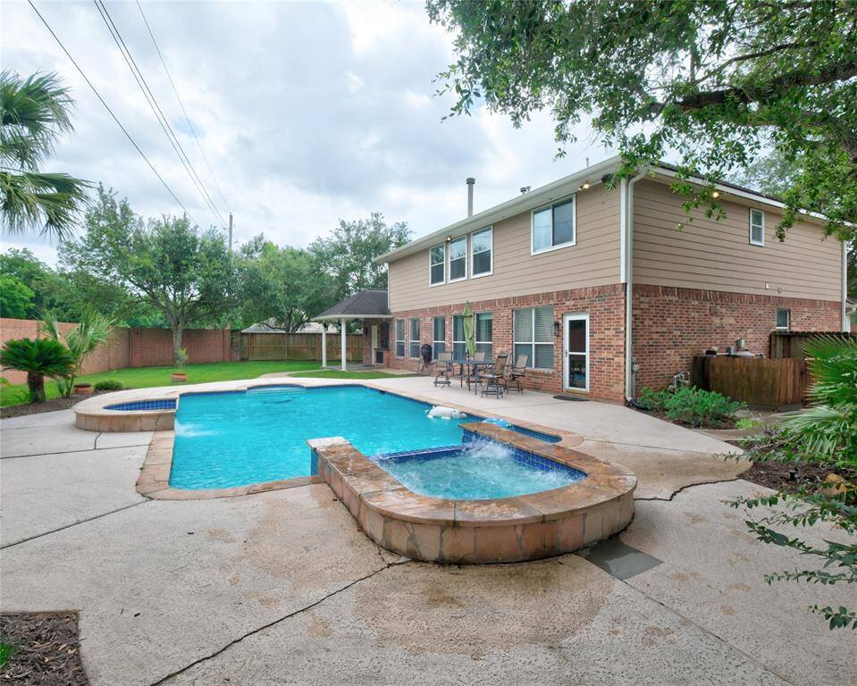 This photo showcases the backyard of a two-story home featuring a spacious swimming pool and hot tub. The area is surrounded by a well-maintained lawn and mature trees, offering a private and inviting outdoor space. A patio with seating provides a perfect spot for relaxation or entertaining.