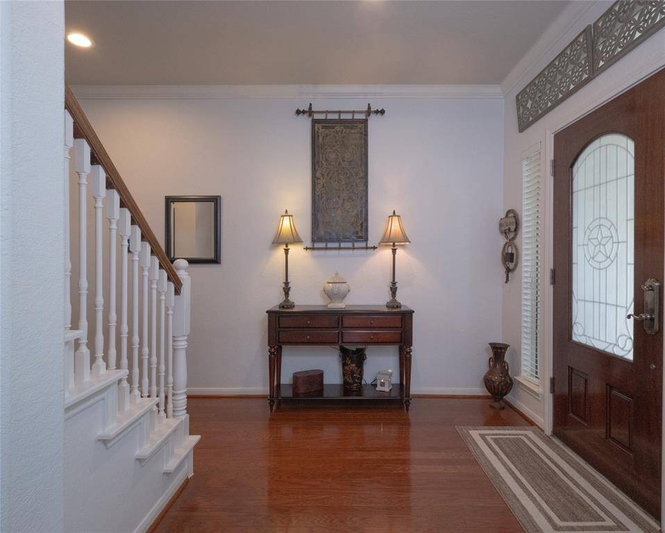 This welcoming entryway features hardwood flooring, a classic wooden staircase, and a decorative front door with glass panels.
