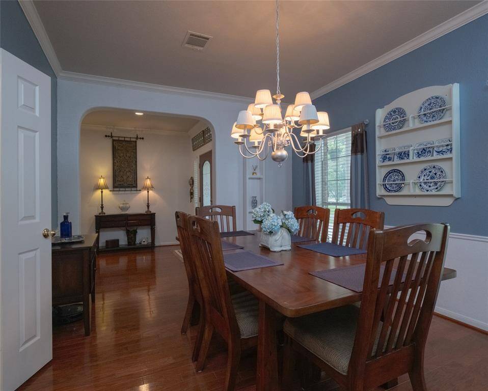 Another view of this gorgeous dining room featuring warm wood flooring, elegant crown molding, and a central chandelier.
