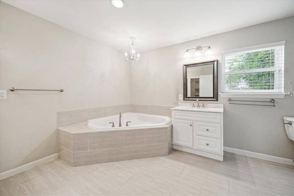 Remodeled in 2014–2015, the primary bath features neutral tile flooring, a jetted soaking tub with chandelier dual updated vanities, and walk-in closet access.