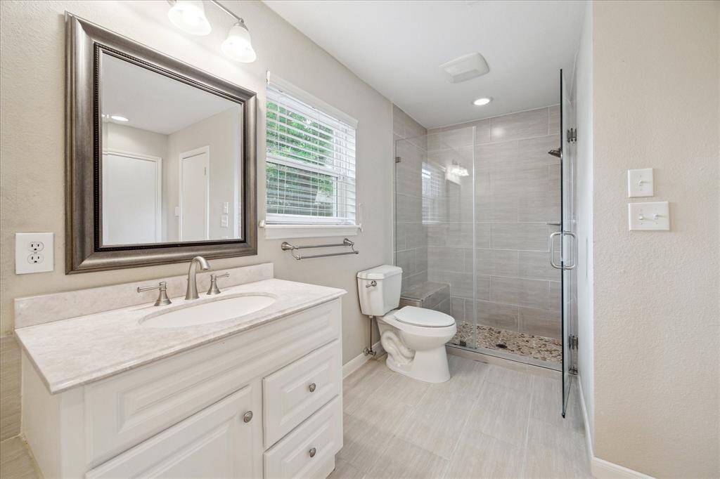 View of the primary bath featuring a frameless glass shower with tile surround and built-in bench. Additional highlights include a large jetted tub, dual vanities, and a walk-in closet.