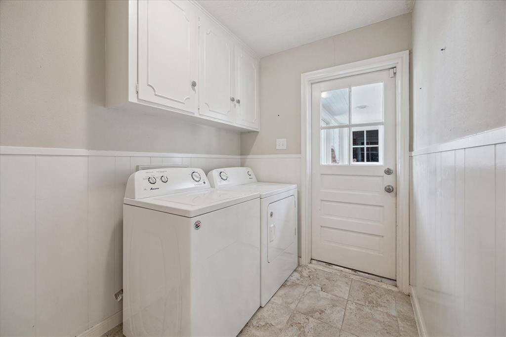 Utility room with full-sized washer and dryer, upper cabinet storage, and tile flooring. The access door leads to the enclosed, air-conditioned breezeway with direct access to the garage and backyard.