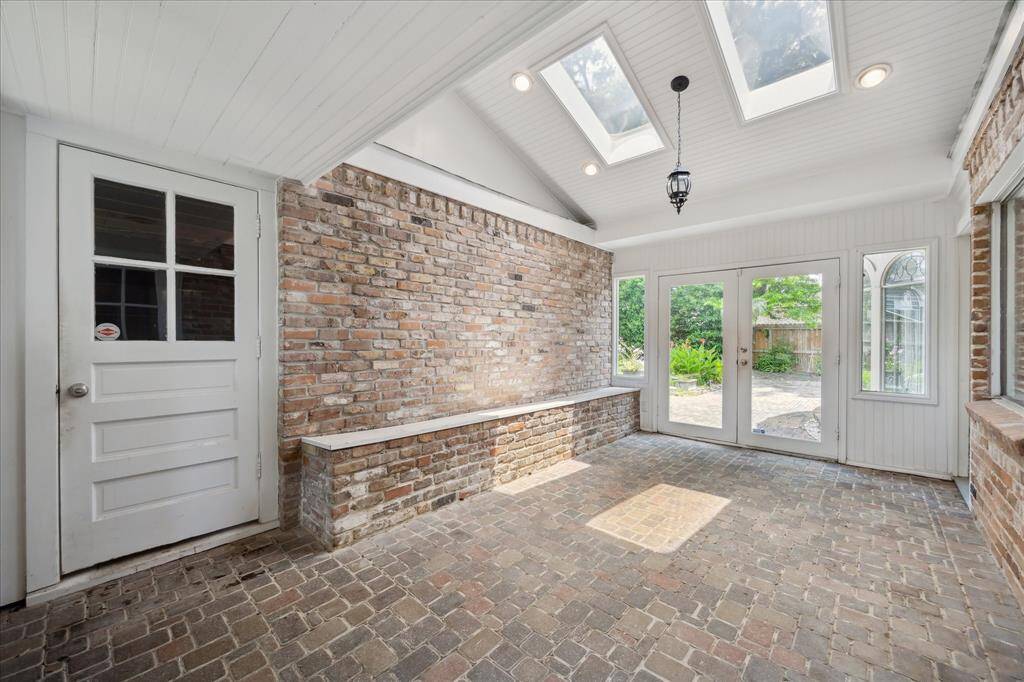Enclosed and air-conditioned breezeway with skylights, brick flooring, and built-in bench seating—connecting the home to the garage and backyard.