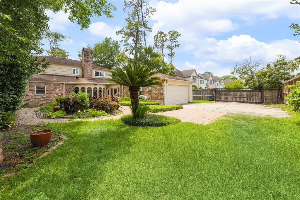 Rear elevation of the home shows the 2-car garage, brick driveway with extra parking, and iron gate set on a spacious corner lot.