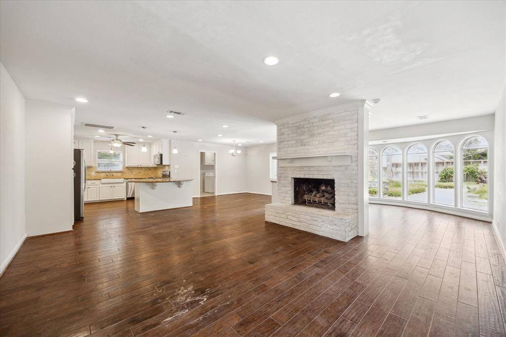 The open-concept first floor layout includes the family room, kitchen, breakfast room, and sunroom highlighted by arched windows, a brick fireplace, and island kitchen with pendant lighting. Ideal for everyday living and entertaining.