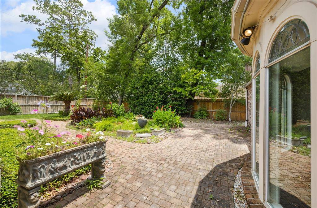 Brick pathways wind through a lush, landscaped backyard with blooming beds and mature trees, offering a spacious retreat with tons of potential for outdoor entertaining or personalization.