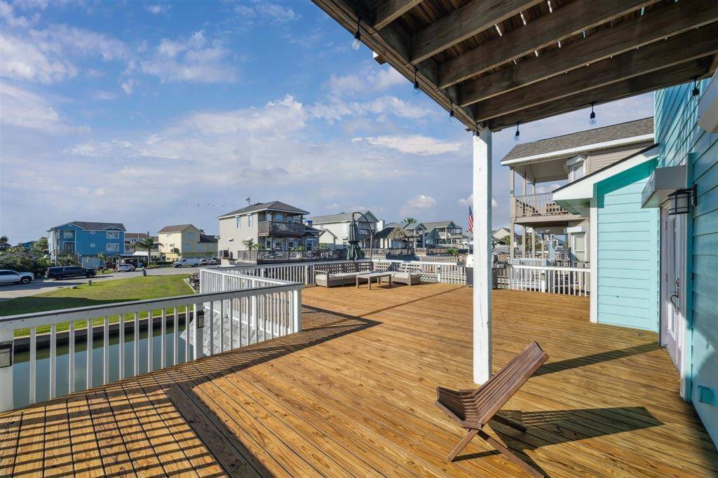 This photo showcases a spacious wooden deck with partial shade from an overhang, offering scenic views of a neighborhood with waterfront homes. Ideal for outdoor relaxation and entertainment.