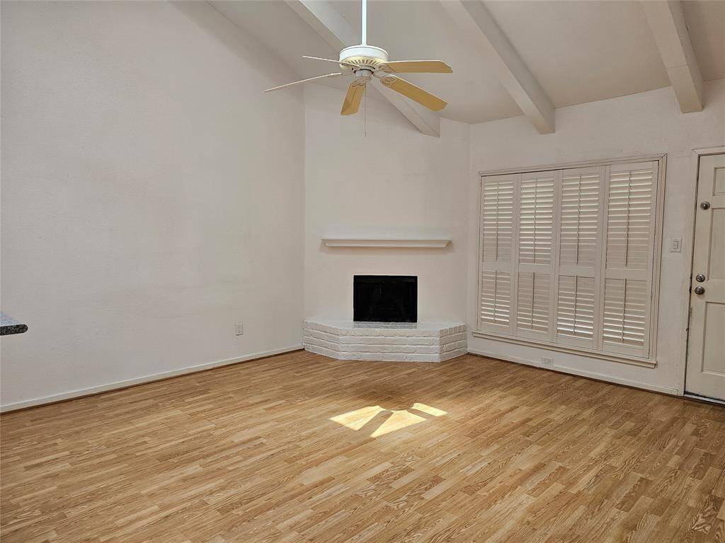 Living room has a wood burning fireplace, cathedral ceiling, fan and shutters on windows
