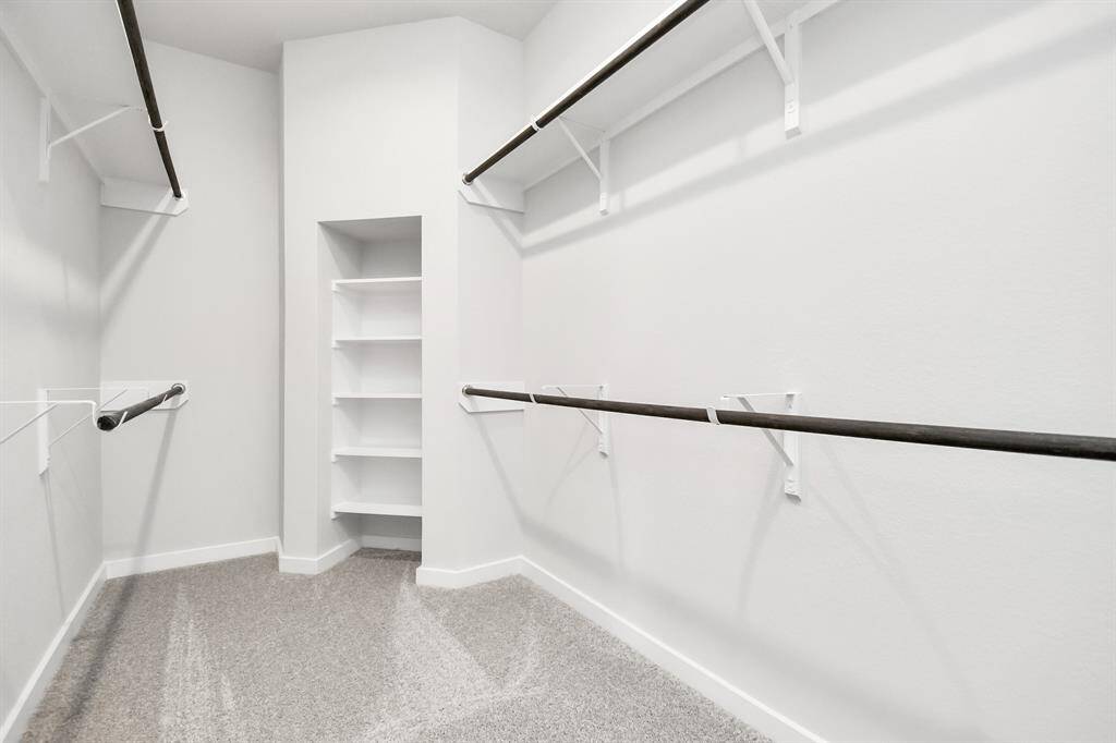 Experience luxury in this spacious walk-in closet with high ceilings and plush carpet. Warm paint tones, built-in shelving, and dark finishes create a contemporary and functional retreat. Sample photo of completed home with similar floor plan. Actual colors and selections may vary.