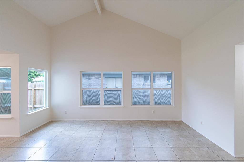 Living room features a high vaulted ceiling and ample natural light from multiple windows, creating an open and airy atmosphere. The neutral tile flooring complements the clean, white walls, offering a versatile space ready for personalization.