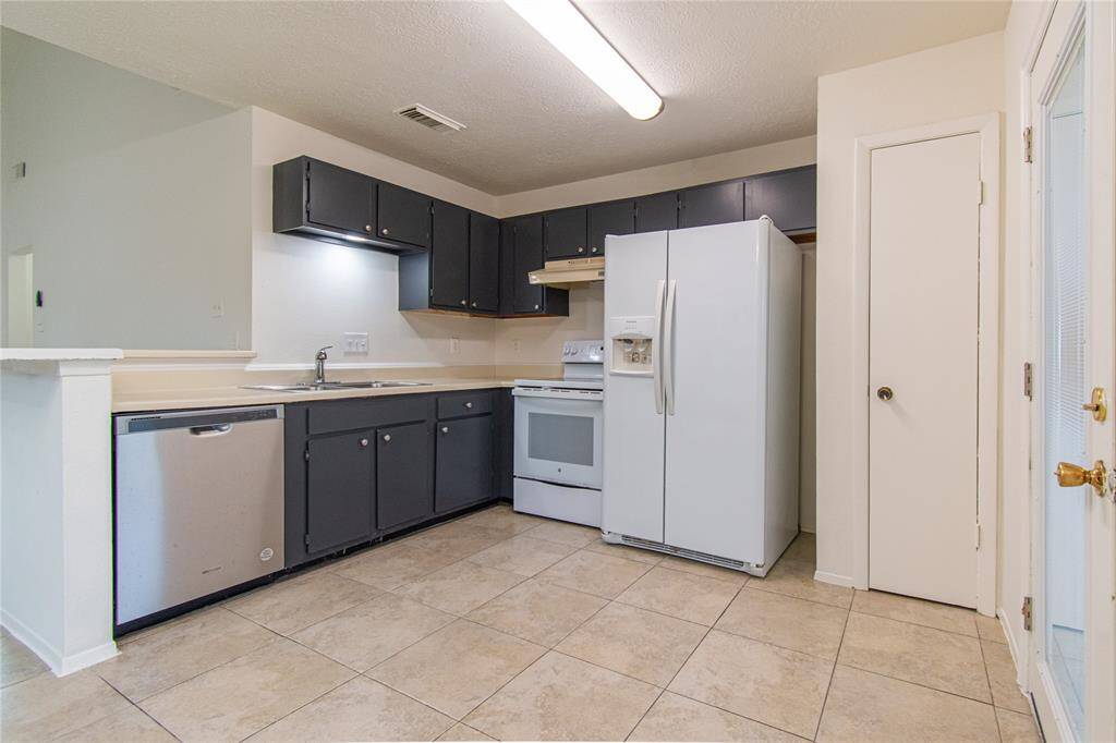 This kitchen features a modern design with dark cabinets, light countertops, and a tile floor. It includes a stainless steel dishwasher, white appliances, and ample storage, creating a functional and stylish cooking space.