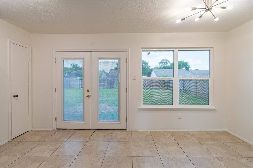 Bright and inviting room with large tiled flooring, featuring double glass doors and a window offering a view of the backyard. Modern lighting adds a stylish touch.